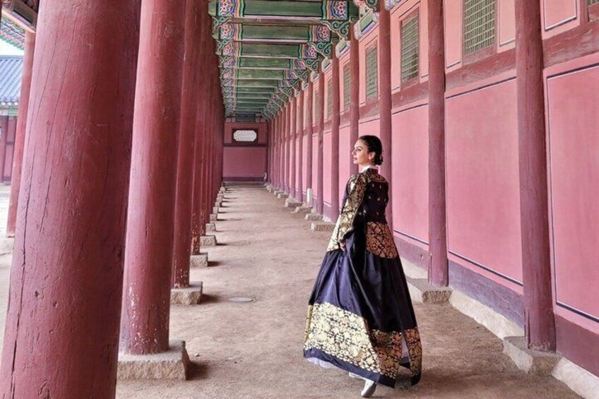 A person in traditional attire walking through a corridor with red columns and patterned ceiling. 5