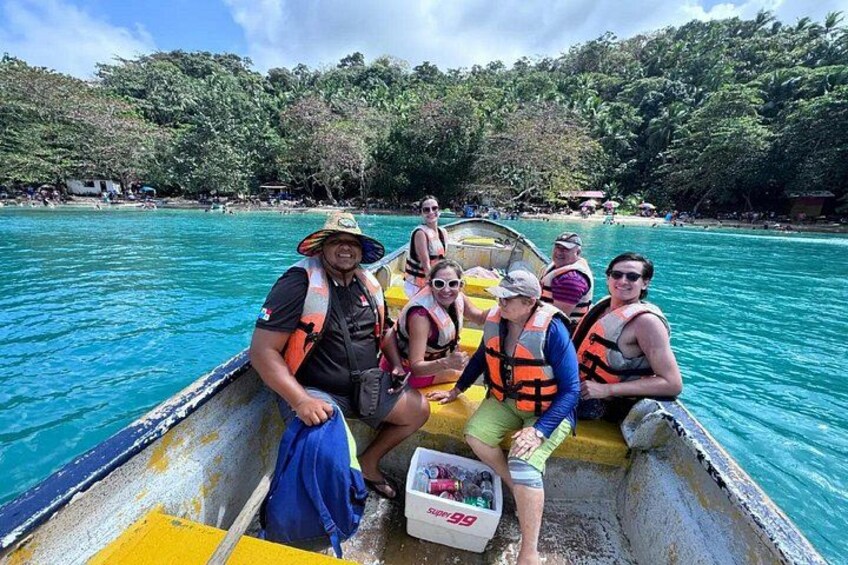 A group of people on a boat in turquoise water, surrounded by lush greenery. 1