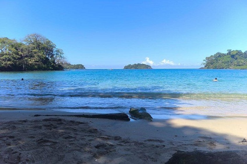 A beach with clear blue water, a sandy shore, and distant islands. 5