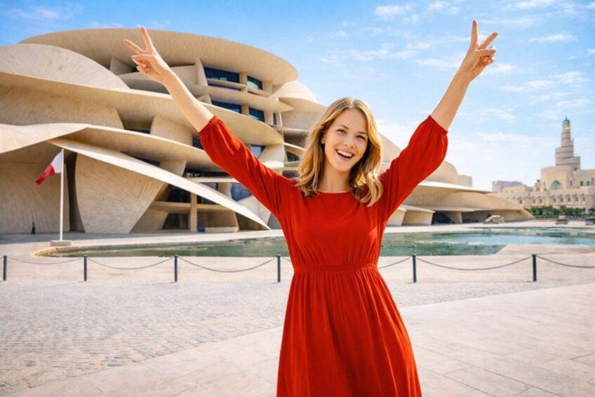Une femme vêtue d’une robe rouge se tient devant un bâtiment d’architecture moderne aux lignes courbes, avec un élément décoratif aquatique en arrière-plan. 1