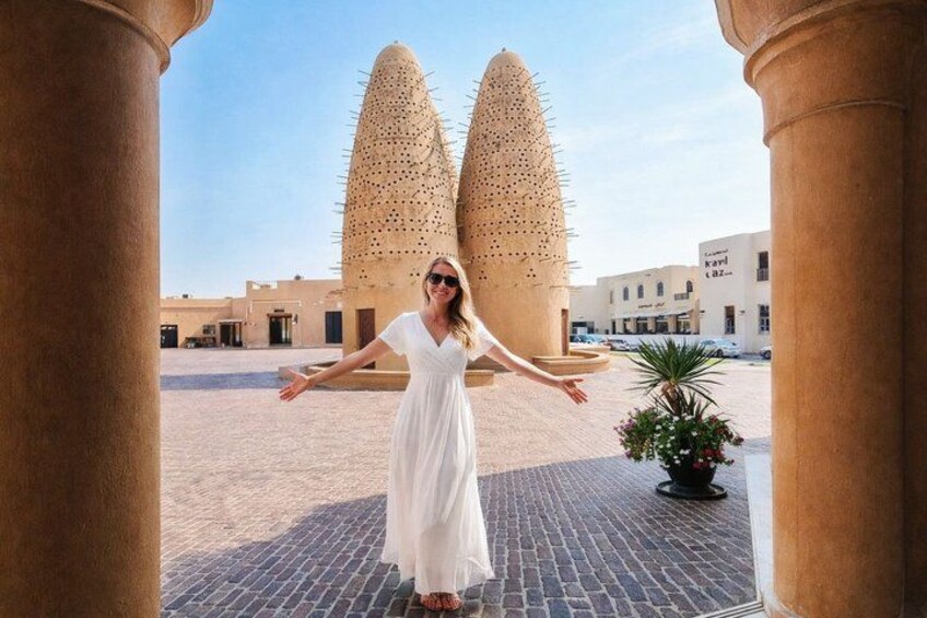 Une femme vêtue d’une robe blanche se tient entre deux grandes structures pointues, dans une cour ouverte. 2