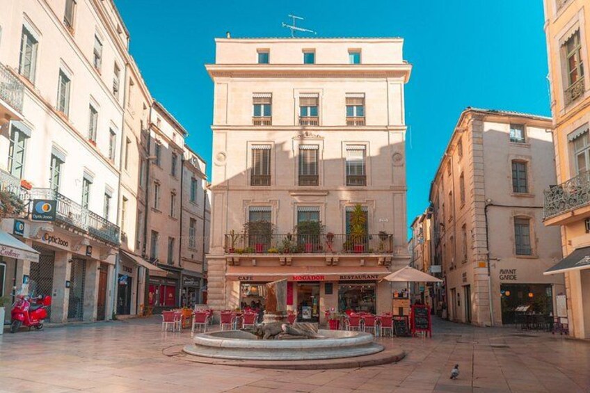 A square with a fountain, cafes, and buildings with balconies. 2