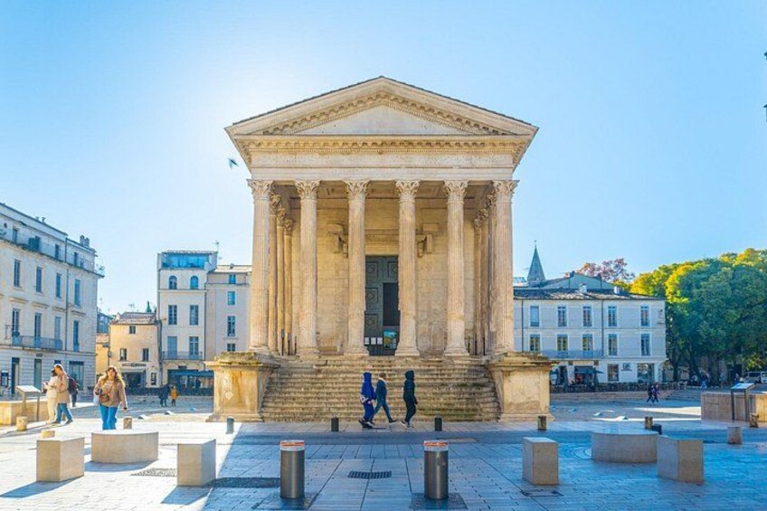 A neoclassical building with columns, surrounded by a plaza with bollards and people walking. 3