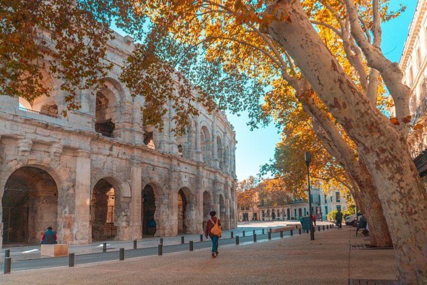 An ancient Roman amphitheater with arches and columns, surrounded by trees with autumn leaves. 5