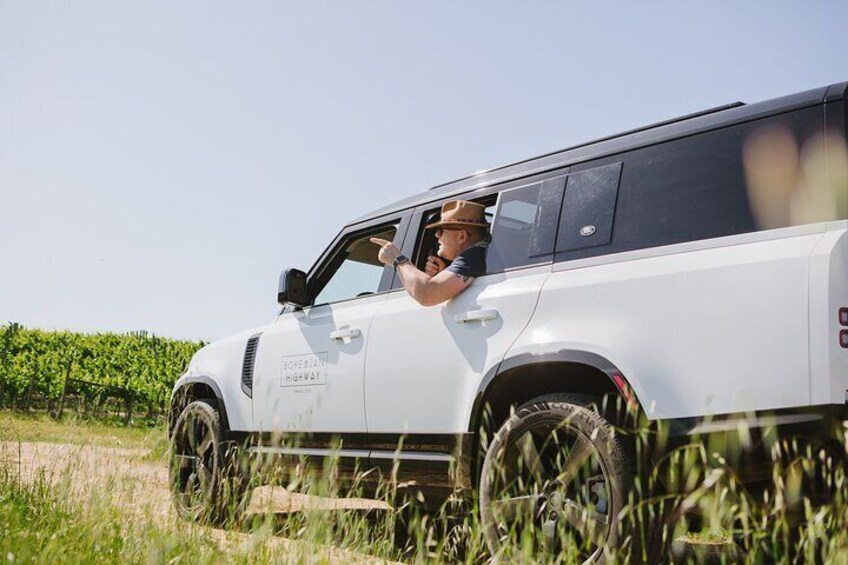 Un SUV blanco en un camino rural, con un conductor que lleva sombrero y gafas de sol. 1
