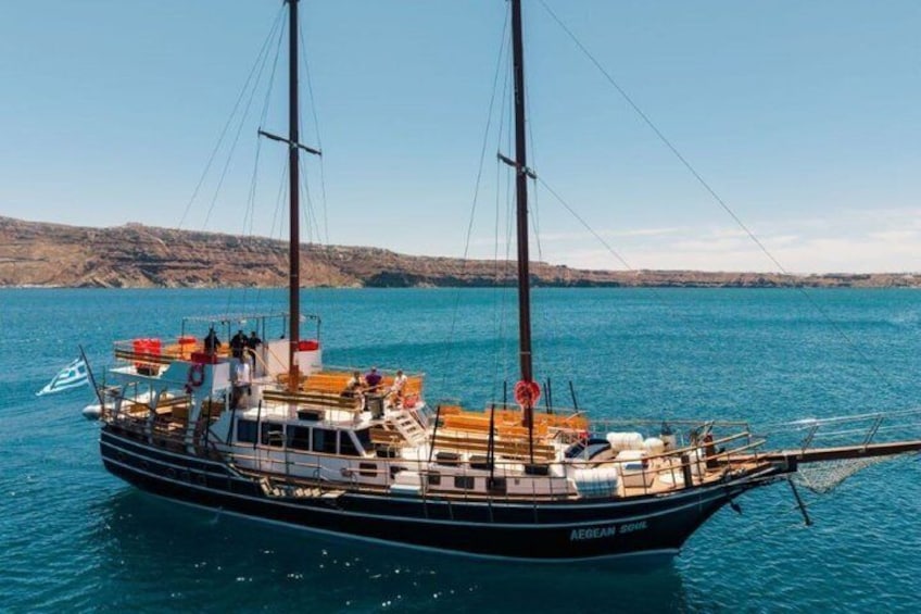 A sailboat named 'Aegean Dawn' on calm waters with a rocky coastline in the background. 1