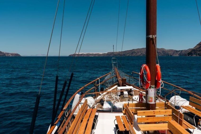 A sailboat with wooden benches and life rings on deck, surrounded by calm blue waters and distant rocky coastline. 4