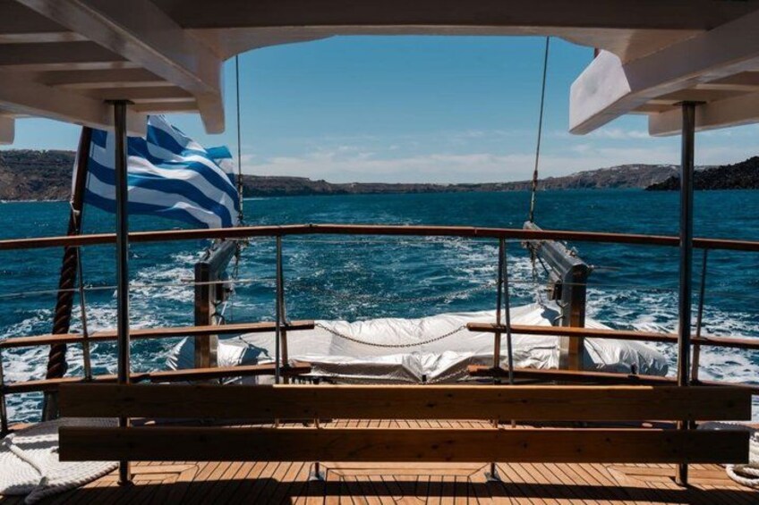 A boat deck with a view of the sea, a flag, and a bench. 2