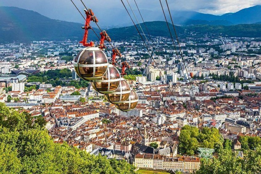 A cable car system with gondolas, a cityscape with red-roofed buildings, and a mountainous backdrop. 3