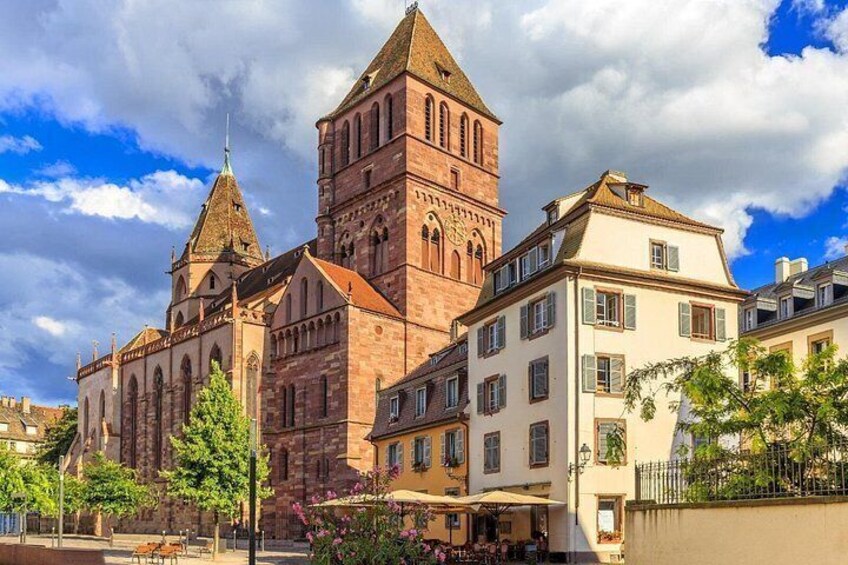A historic building with a prominent tower, adjacent modern buildings, and a clear sky. 2