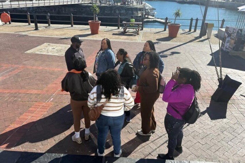 Un grupo de personas de pie en una zona pavimentada, con una masa de agua y un columpio al fondo. 4