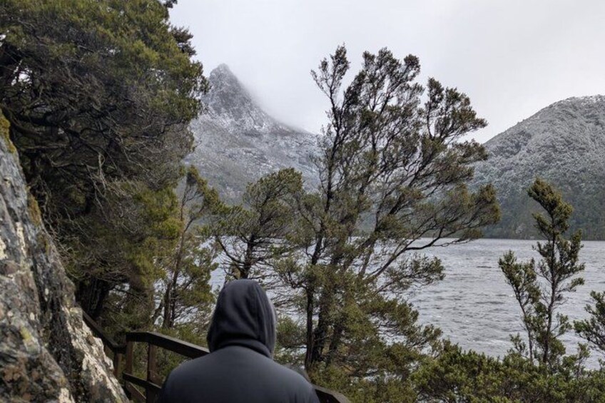 A person in a hoodie overlooking a lake with trees and mountains in the background. 4