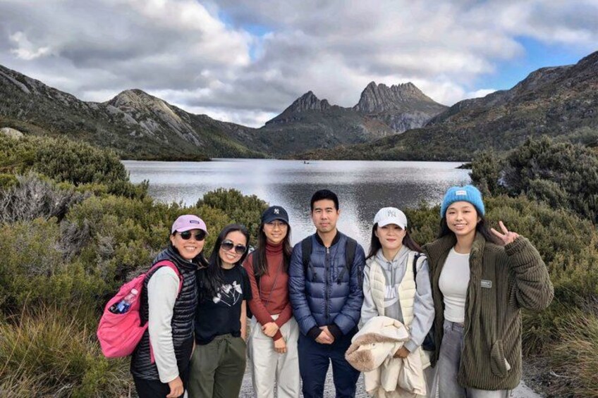 A group of people standing in front of a lake with mountains in the background. 1