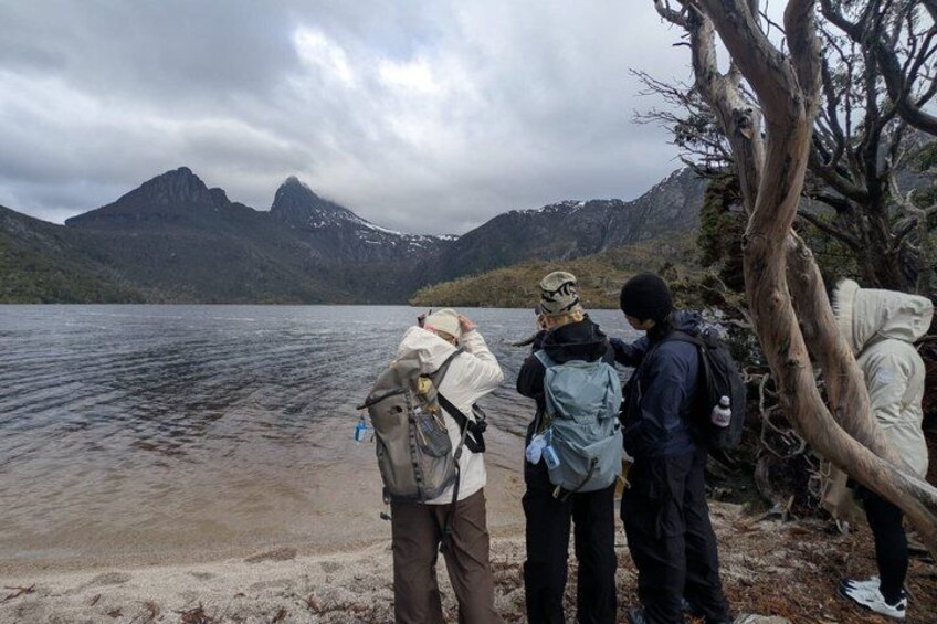 A group of people standing by a lake with mountains in the background. 2