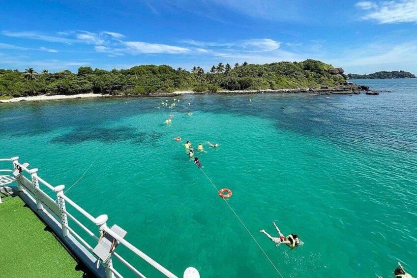 A clear turquoise sea with a boat, people swimming, and a green island in the background. 5