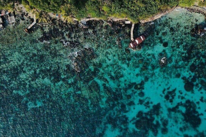 An aerial view of a coastal area with clear turquoise waters, rocky outcrops, and a small structure with a red roof. 2