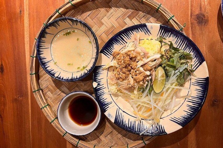 A meal with a bowl of soup, a plate of noodles with vegetables and meat, and a small bowl of sauce. 3