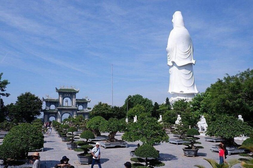 A large white statue, a pagoda, and a well-maintained garden with potted plants. 1