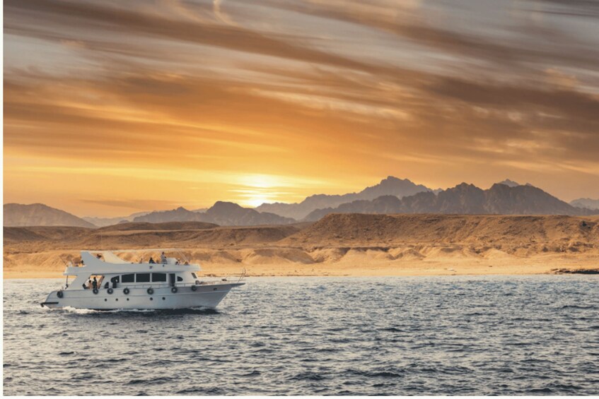 A boat on calm waters with a sunset and mountains in the background. 2