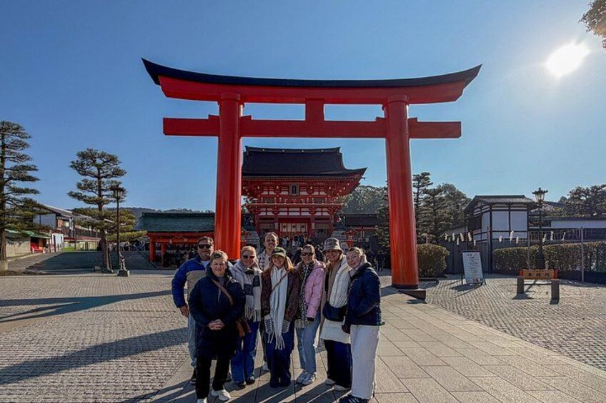 En gruppe mennesker står foran en rød torii-port med en traditionel bygning i baggrunden. 5