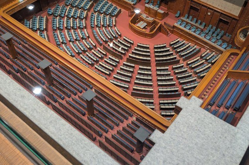 A grand hall with tiered seating, a central stage, and ornate wood paneling. 3