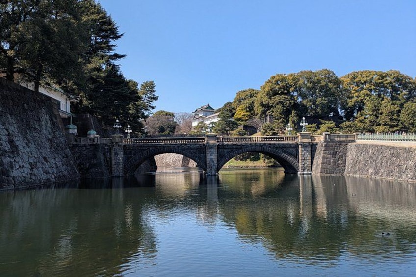 A stone bridge over a calm river, surrounded by trees and buildings. 2