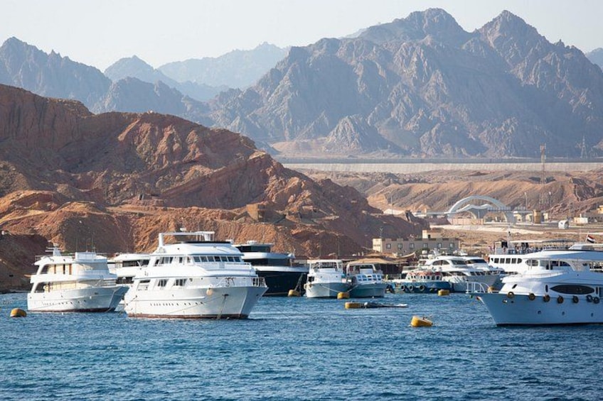A marina with several white yachts docked, surrounded by rocky terrain and mountains in the background. 4