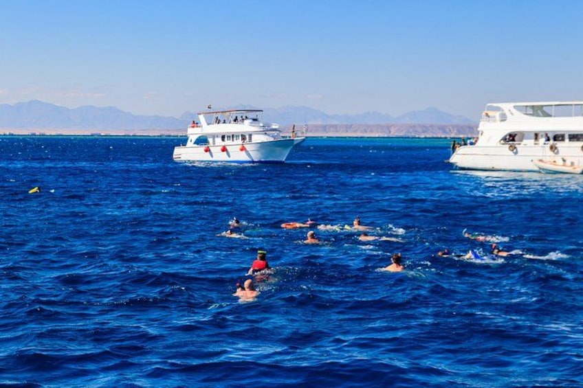 A group of people swimming in the ocean, with two boats in the background. 2