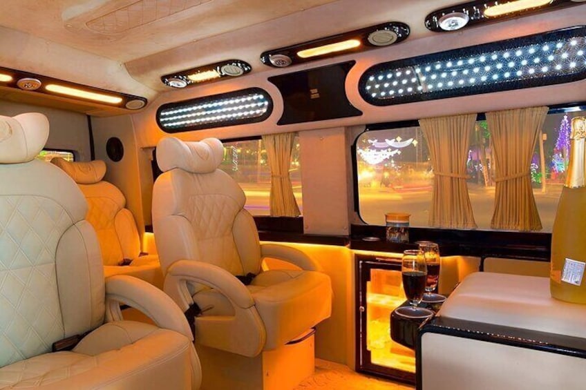 A luxurious train interior with plush leather seats, ambient lighting, and a small table with a bottle and glasses. 1