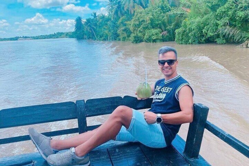 A person sitting on a bench by a river, holding a drink. 5