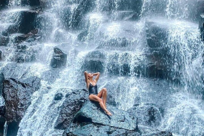 Eine Person sitzt auf Felsen neben einem Wasserfall. 1