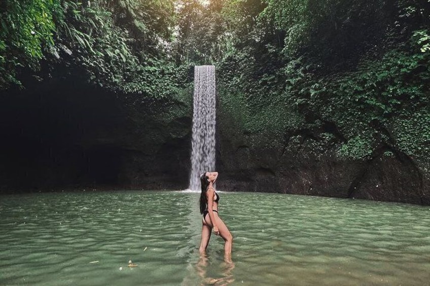 A person standing in water with a waterfall in the background. 1