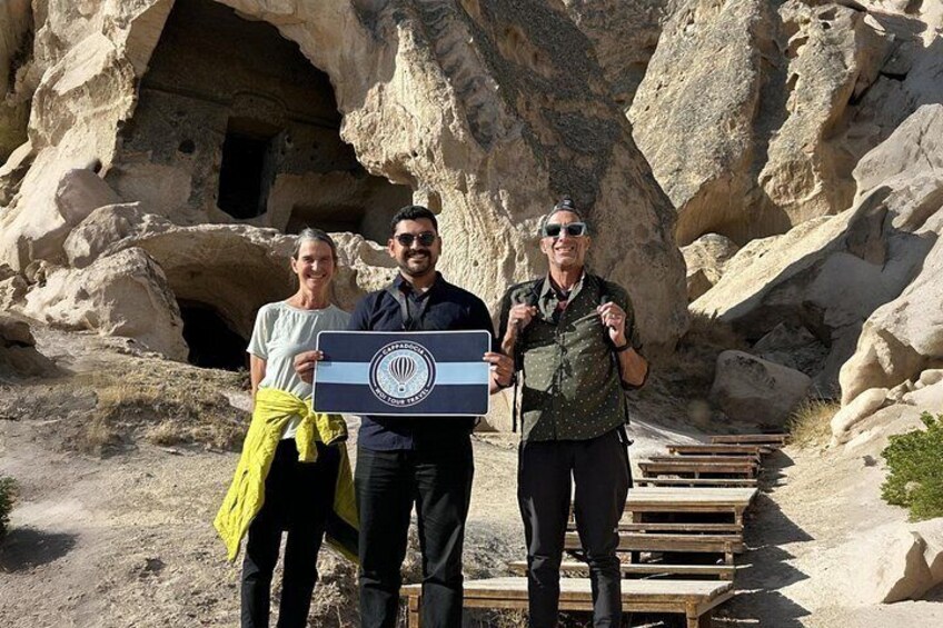 Tres personas de pie frente a una cueva con un pasillo de madera. 1