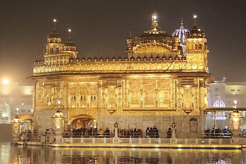 A brightly lit historic building with intricate architecture, a reflective water body in front, and a crowd of people around it. 2