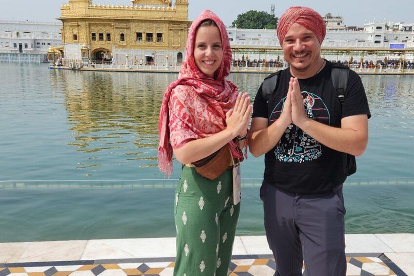 Two people standing by a body of water with a golden temple in the background. 5