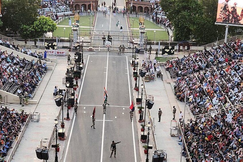 A parade with participants marching down a wide street, spectators lining the sides, and a large crowd watching from stadium seating. 3