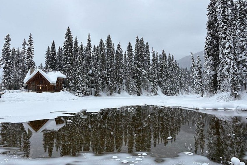 Une cabane entourée d’arbres couverts de neige et d’un lac gelé. 5