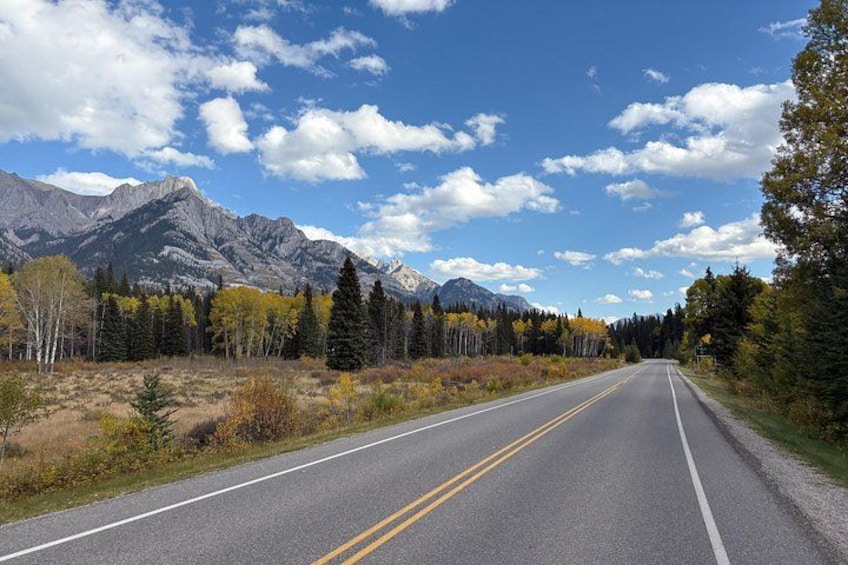 Une route à deux voies, avec des montagnes en arrière-plan et des arbres aux couleurs automnales de chaque côté. 4