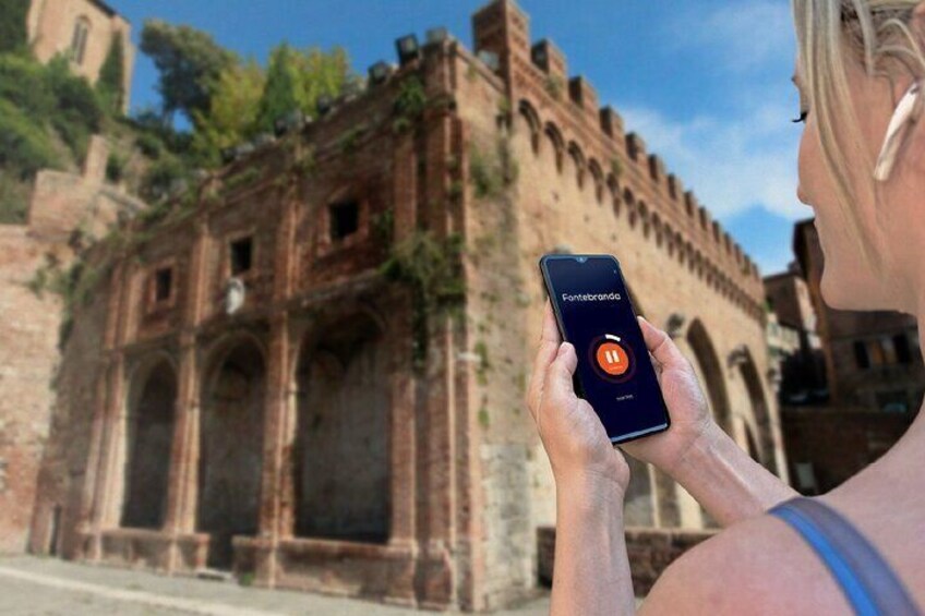A person using a smartphone with an app named "Fontesbrando" in front of an ancient stone structure. 5