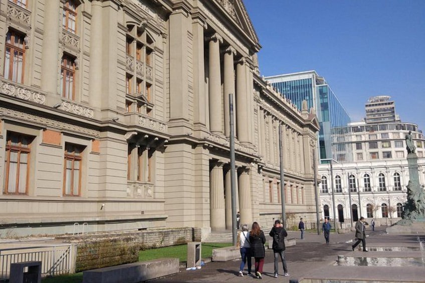 Ein historisches Gebäude mit klassischer Architektur, im Hintergrund ein modernes Glasgebäude und eine nasse Straße. 3