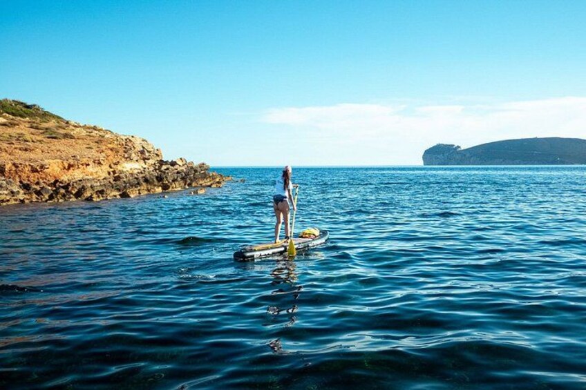 Una persona fa paddleboard su un mare calmo, con una costa rocciosa e cielo sereno. 3
