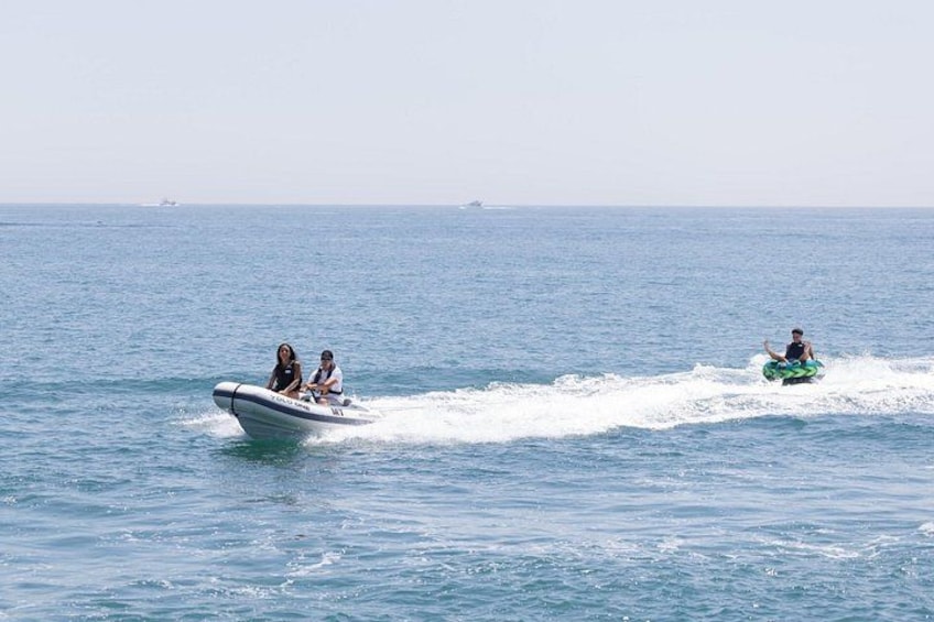 Una persona montando un jet ski sobre el agua, otra persona en un bote y una tercera persona en un flotador acuático. 4
