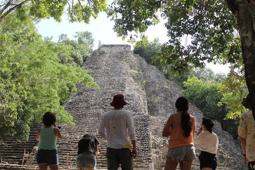 Un grupo de personas observando una gran pirámide antigua rodeada de árboles. 1