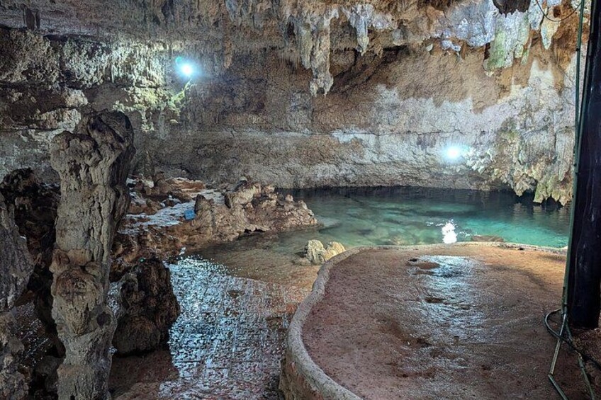 Interior de una cueva con estalactitas, un estanque de agua y una estructura circular de piedra. 3