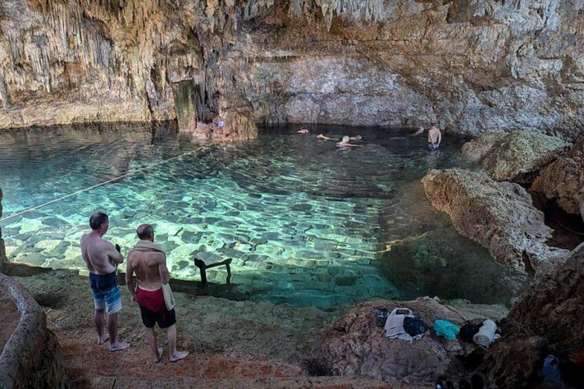 Una cueva con una piscina cristalina, paredes rocosas y personas nadando. 4