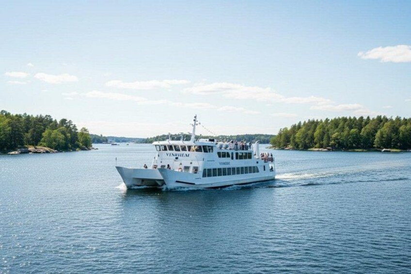 A white boat named 'VINHILIM' on a calm body of water with a forested shoreline in the background. 2