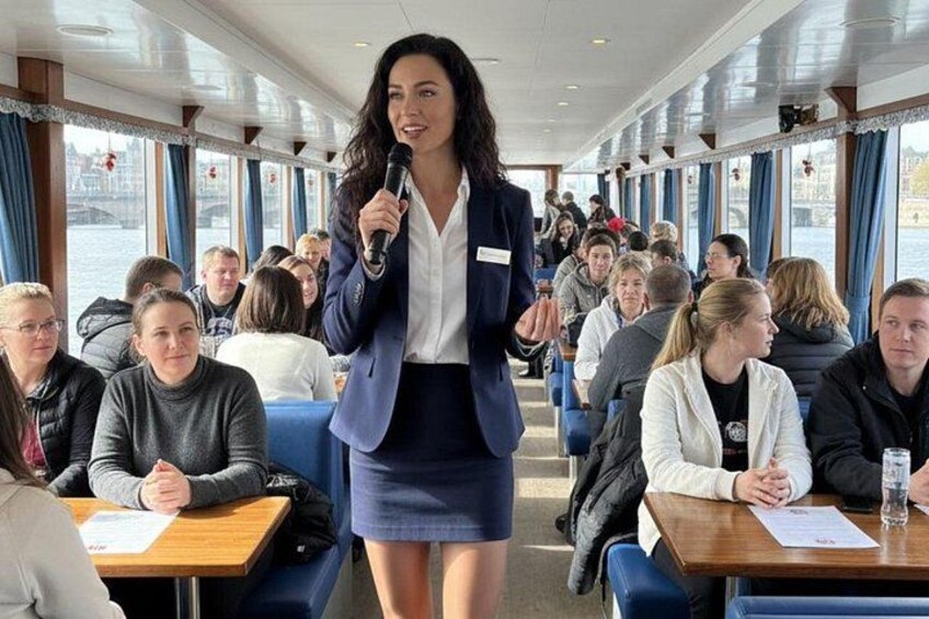 A woman speaking to a group of seated people on a boat. 4
