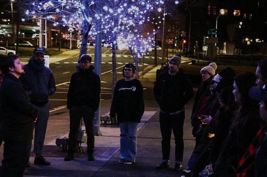 Un grupo de personas de pie en una acera de noche, con árboles adornados con luces. 2