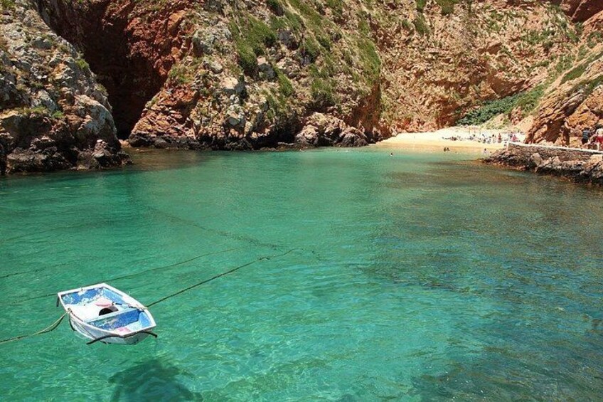 Un bateau à la dérive sur une eau turquoise et limpide, une côte rocheuse et une plage de sable où se trouvent des gens. 5
