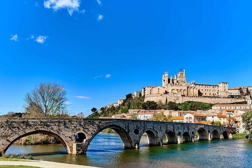 A stone bridge over a river, a historic building on a hill, and clear blue sky. 1
